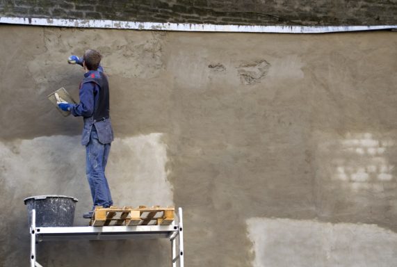 Handwerker verputzt wall mit einer Kelle auf einem Gerüst.