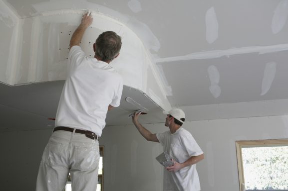 Zwei Männer streichen eine Decke in einem Raum.