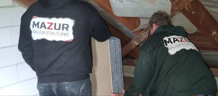 Zwei Männer in Arbeitskleidung verlegen Materialien im Dachboden.