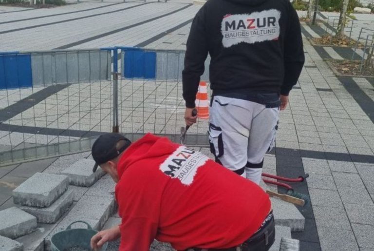 Arbeiter der Firma Mazur Baugestaltung befestigen Steine auf einem Bürgersteig.