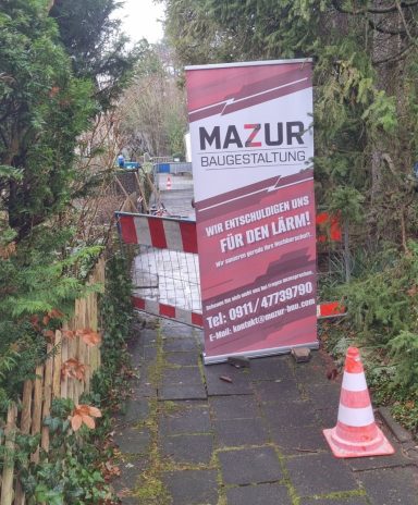 Baustellenbanner mit Warnschildern und umgestürztem Verkehrshütchen im Gartenweg.