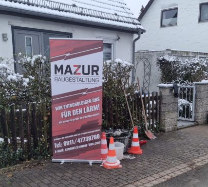 Banner für Mazur Dienstleistungen neben einem Wohnhaus, mit Schaufel und Verkehrshütchen.